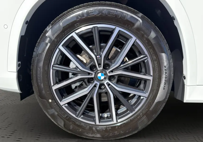 Gros plan sur la roue avant droite d’un BMW X1 blanc avec jante alliage M Sport et pneu Nexen.