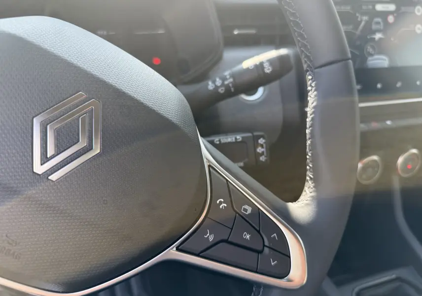 Gros plan sur le volant cuir avec commandes intégrées de la Renault Clio 1.5 DCI 100CH Evolution, tableau de bord en arrière-plan.