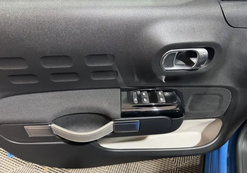 Vue rapprochée de la porte avant gauche de la Citroën C3 bleu, avec commandes de vitres et poignée intérieure chromée.