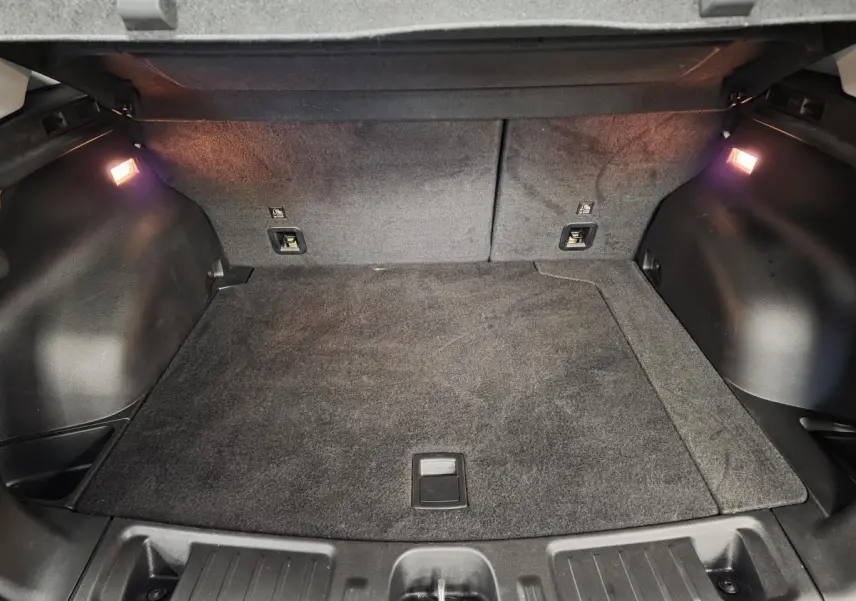 Coffre ouvert du Jeep Compass blanc 2024, vue intérieure montrant le tapis de sol et éclairage latéral.