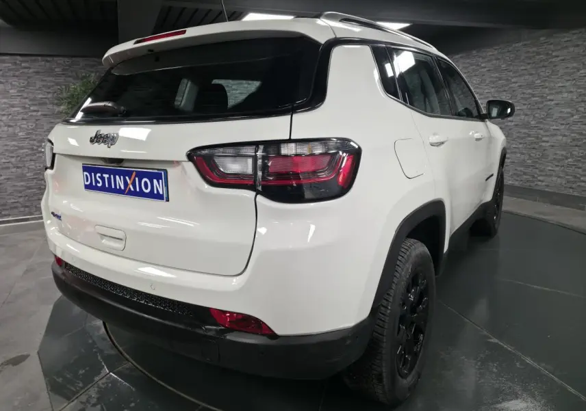 Vue 3/4 arrière droite d'un Jeep Compass blanc 2024 avec jantes noires et toit blanc en intérieur showroom.