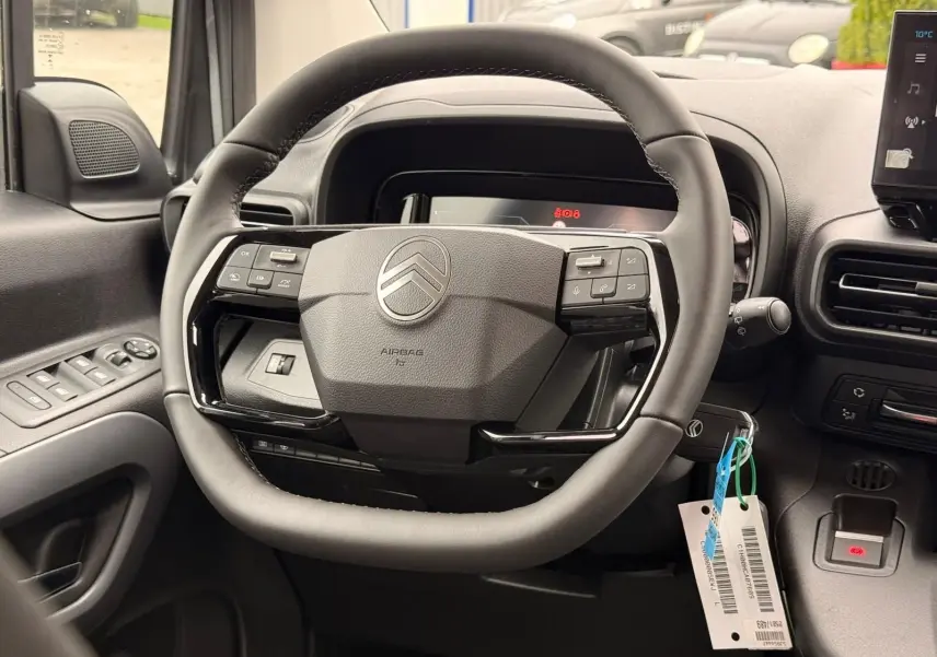 Vue rapprochée du volant cuir noir du Citroën Berlingo 2025, avec commandes intégrées et tableau de bord numérique.