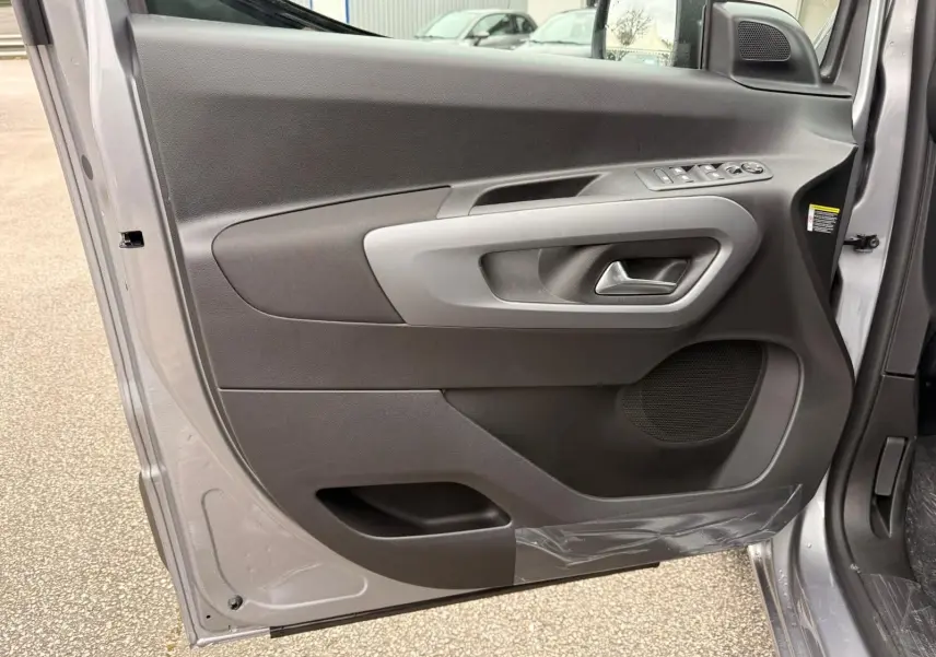 Vue intérieure de la porte avant gauche du Citroën Berlingo gris Artense, avec commandes électriques et poignée intégrée.