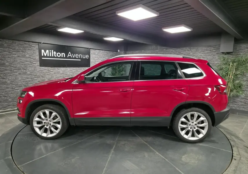 Profil droit d'un Skoda Karoq rouge avec jantes alliage 19 pouces dans un showroom intérieur.