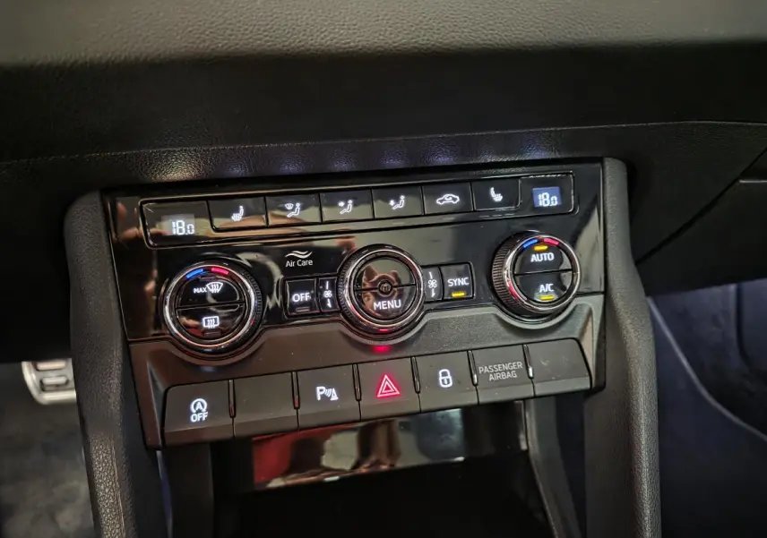 Panneau de commande de climatisation noir brillant dans l'habitacle d'une Skoda Karoq rouge, avec réglages digitaux à 18°C.