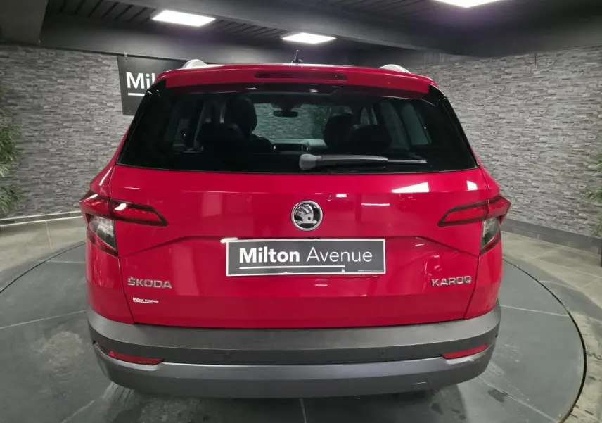 Vue arrière d'un Skoda Karoq rouge avec logo et plaque Milton Avenue dans un showroom intérieur.