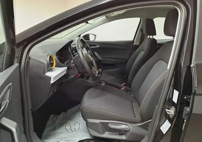 Intérieur côté conducteur du SEAT Ibiza 2024 noir minuit, vue de profil montrant sièges et tableau de bord avec airbag jaune.