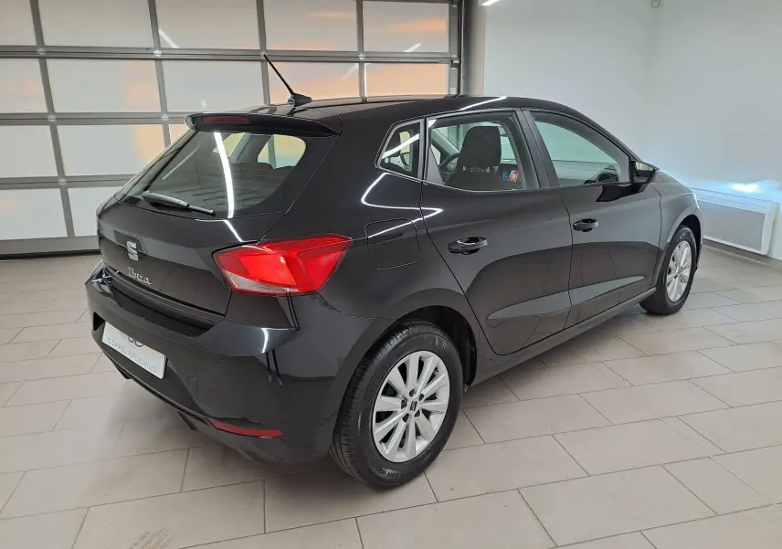 Vue 3/4 arrière droite d'une SEAT Ibiza 2024 noir minuit, avec feux arrière rouges et jantes argentées en intérieur showroom.