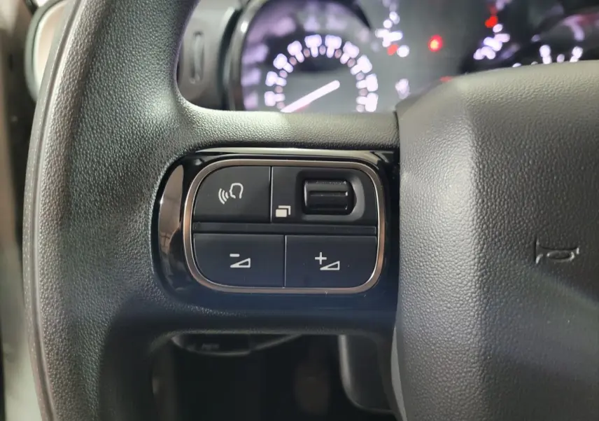 Gros plan sur les commandes gauche du volant noir de la Citroën C3 2022, avec tableau de bord flou en arrière-plan.