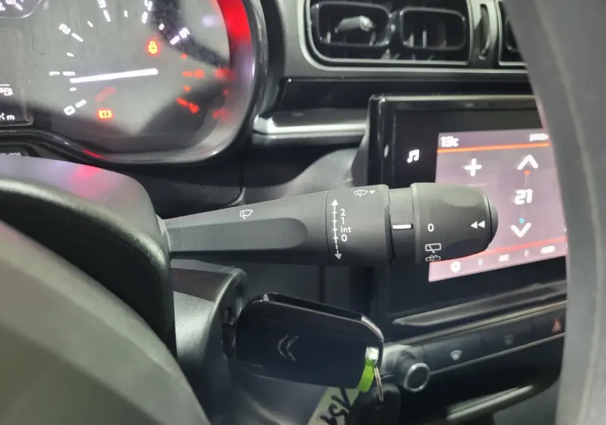 Gros plan intérieur sur la commande d’essuie-glaces à gauche du volant d’une Citroën C3 beige, avec tableau de bord et écran tactile visible.