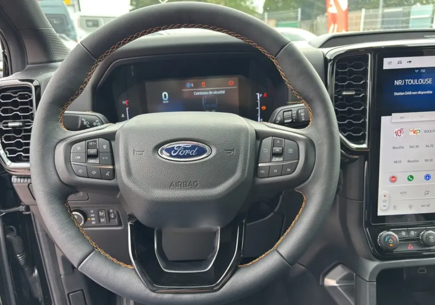 Vue rapprochée du volant cuir noir avec surpiqûres orange du Ford Ranger 2025 et tableau de bord numérique.