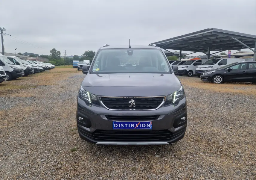 Vue frontale d'un Peugeot Rifter gris platinium 2019 avec feux allumés sur un parking extérieur.