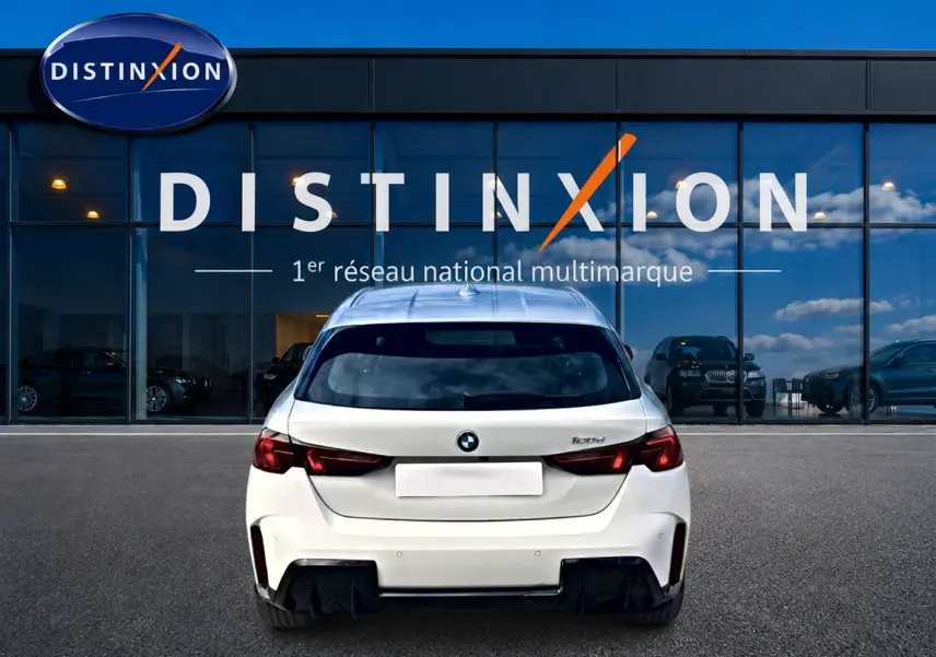 Vue arrière d'une BMW Série 1 blanche pure (120da M Sport) garée devant une vitrine avec logo Distinxion.