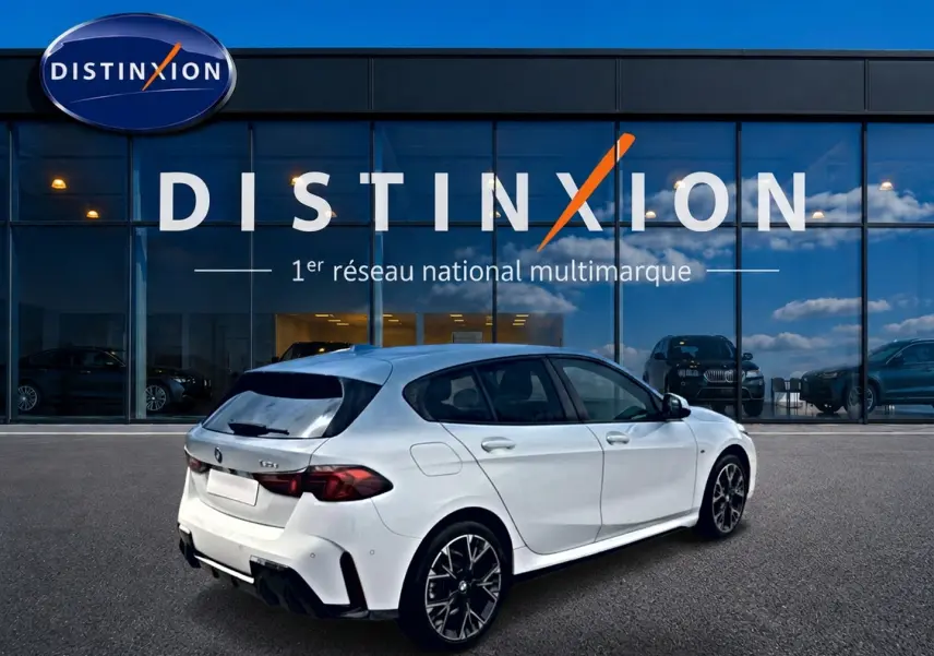BMW Série 1 blanche vue en 3/4 arrière droit, avec jantes sport et feux arrière LED sombres, devant une vitrine Distinxion.