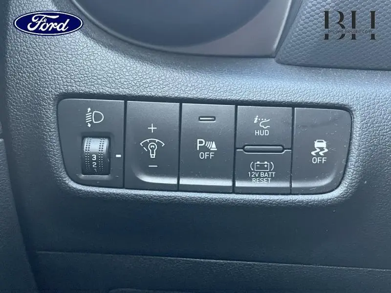 Panneau de commandes noires avec réglage phares, assistance parking, HUD et contrôle de stabilité dans un Hyundai Kona rouge.