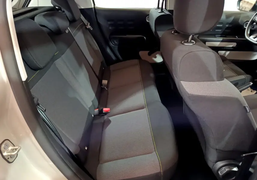 Vue intérieure côté arrière gauche de la Citroën C3 beige 2022, montrant la banquette arrière et les sièges avant en tissu noir.