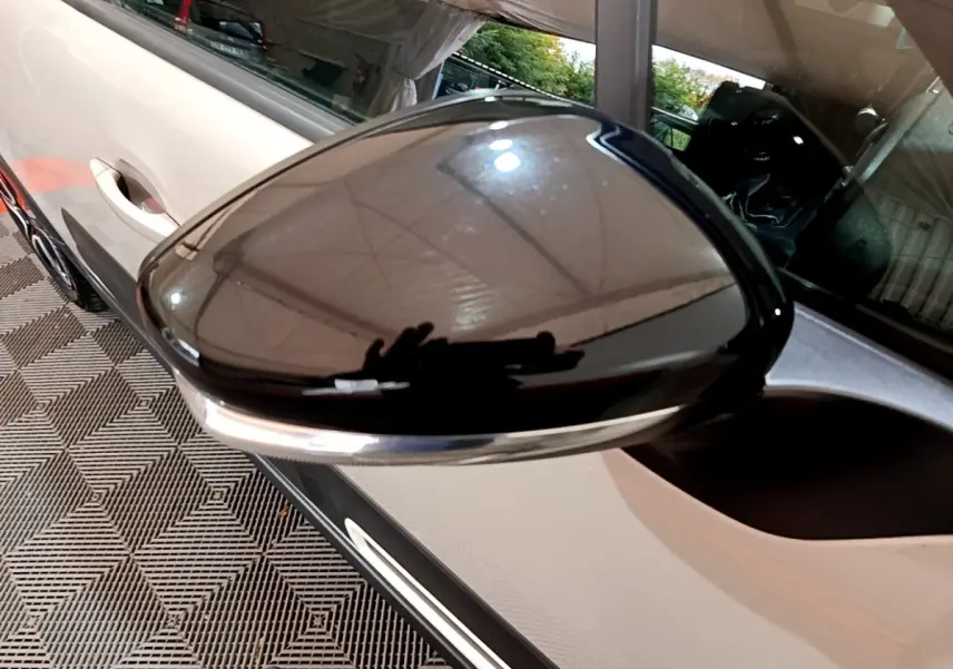 Rétroviseur noir brillant côté conducteur d'une Citroën C3 beige vue de près, avec poignée de porte visible.