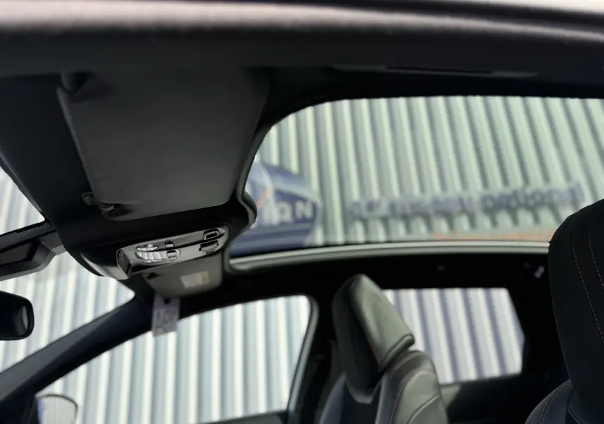 Vue intérieure du toit ouvrant panoramique et des sièges avant noirs avec surpiqûres rouges d'une Peugeot 308 SW blanc nacré 2021.