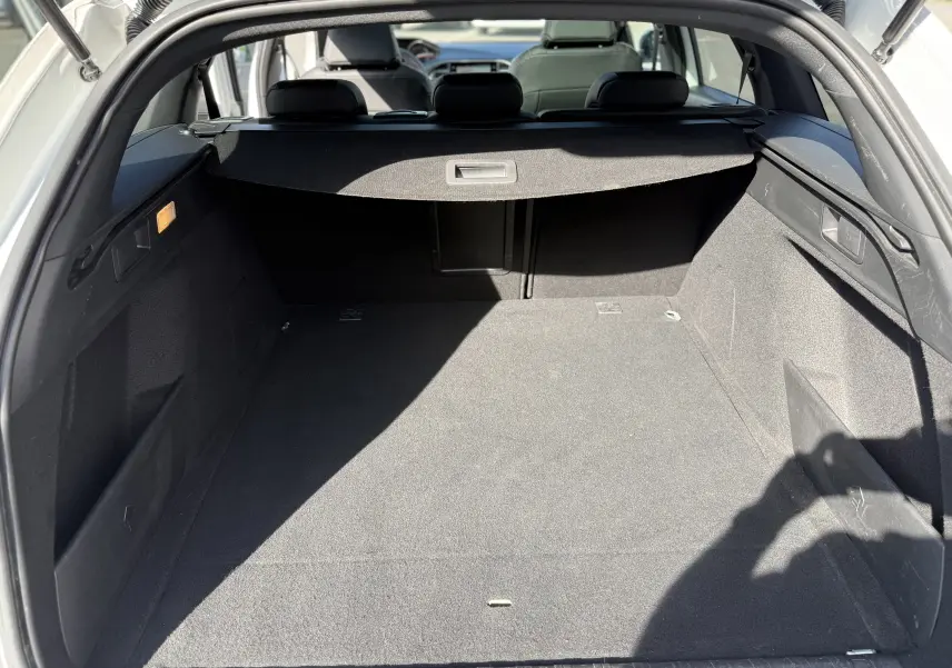 Vue intérieure du coffre spacieux d'une Peugeot 308 SW blanc nacré, avec cache-bagages et sièges arrière visibles.