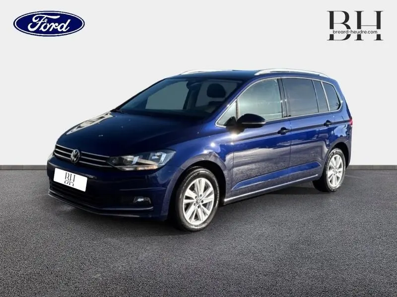 Volkswagen Touran bleu Atlantique métallisé vu en 3/4 avant droit avec jantes alu et barres de toit.