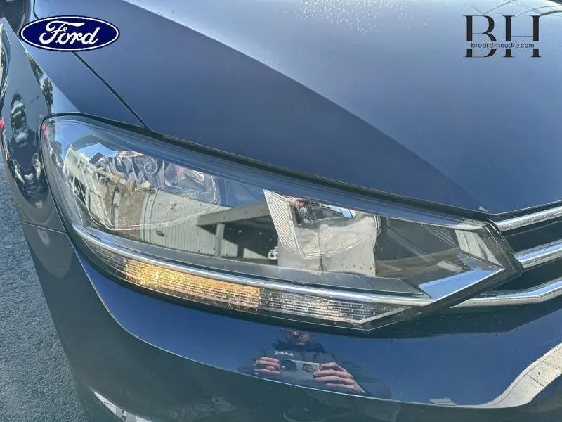 Gros plan sur le phare avant gauche d’un Volkswagen Touran bleu Atlantique métallisé avec calandre chromée.