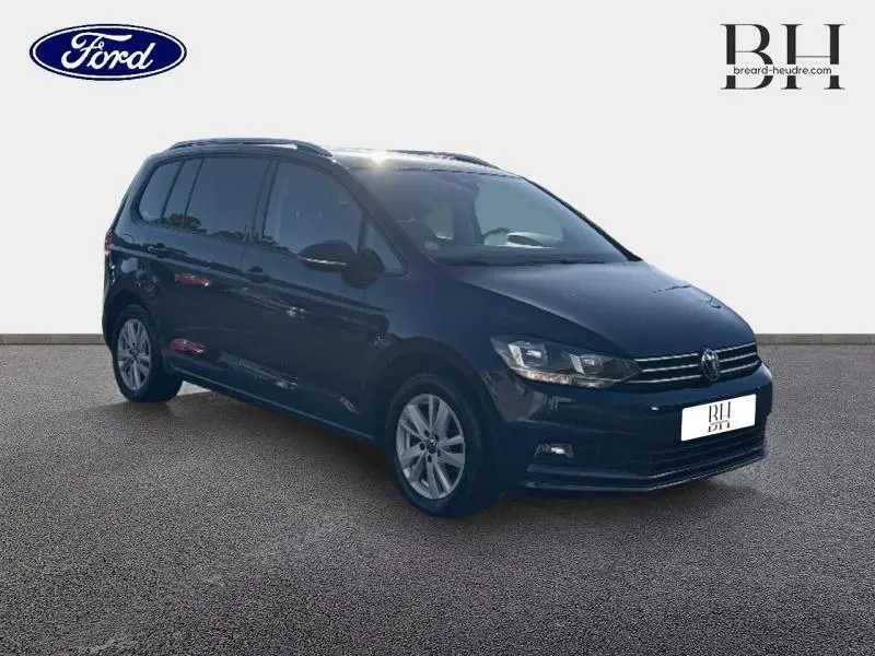 Volkswagen Touran bleu Atlantique métallisé vu en 3/4 avant droit avec jantes alu et barres de toit.