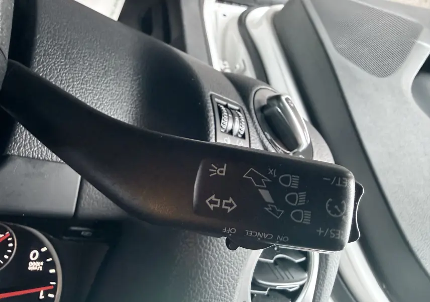 Gros plan sur le commodo de clignotants du Volkswagen Tiguan 2.0 TDI blanc, avec tableau de bord et aérateurs visibles.