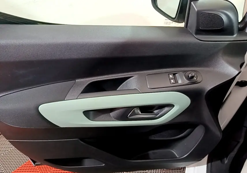 Vue intérieure côté conducteur de la porte d’un Citroën Berlingo blanc, avec poignée grise et commandes électriques.
