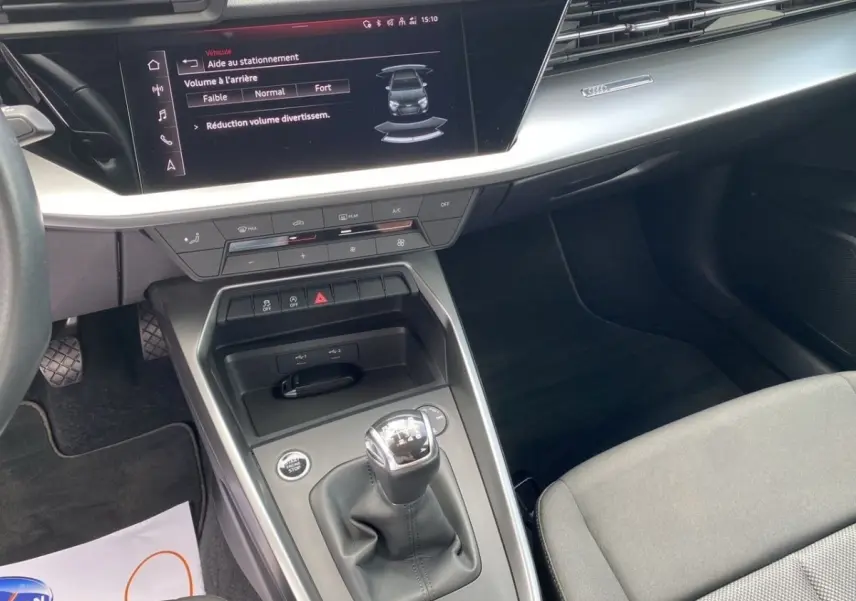 Vue intérieure centrée sur la console centrale d'une Audi A3 gris foncé, avec levier de vitesses manuel et écran tactile.