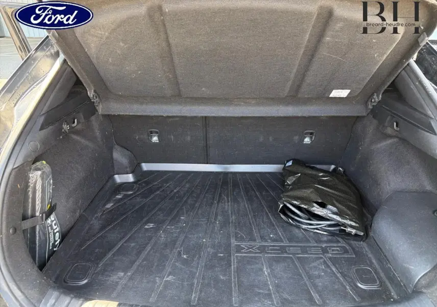 Vue intérieure du coffre ouvert d'un KIA Xceed noir Basalte, avec tapis de coffre marqué Xceed et câble de recharge plié.
