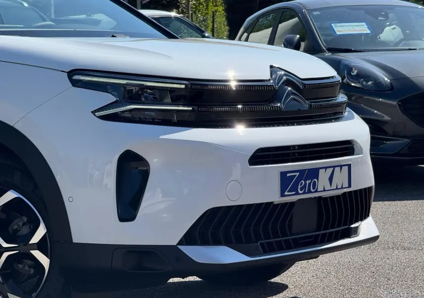 Vue 3/4 avant droite du Citroën C5 Aircross blanc banquise avec calandre noire et plaque Zero KM visible.