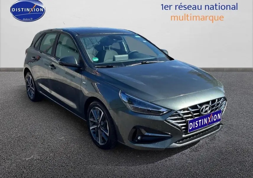 Hyundai i30 gris argent vue 3/4 avant droit avec calandre chromée et jantes alliage distinctives.