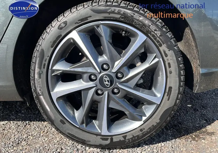 Gros plan sur la jante alu grise et le pneu tout temps du côté gauche d'une Hyundai i30 gris argent 2024.