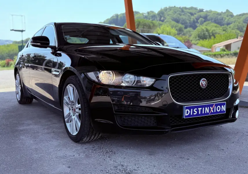 Jaguar XE noir vue 3/4 avant droit sous abri, avec calandre distinctive et phares allumés.