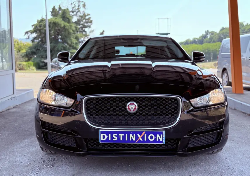 Vue frontale d'une Jaguar XE noire avec calandre distinctive et phares allumés sous un abri.