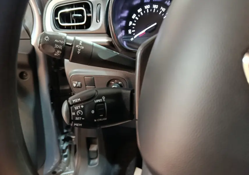 Gros plan sur la colonne de direction et commandes du volant d’une Citroën C3 gris foncé, tableau de bord partiellement visible.