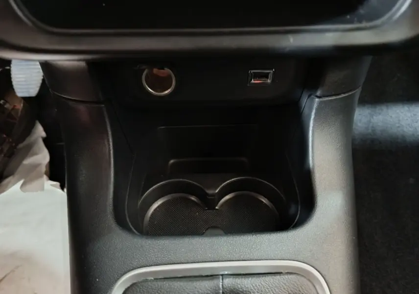 Gros plan intérieur sur la console centrale noire avec prise 12V, port USB et porte-gobelets de la Citroën C3 2024.