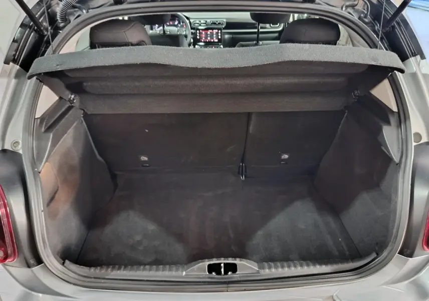 Coffre ouvert vu de l'arrière d'une Citroën C3 gris foncé 2024, intérieur noir et tablette de coffre relevée.