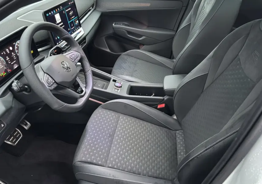 Vue intérieure côté conducteur du Volkswagen T-Roc 2026, sièges tissu gris foncé et tableau de bord digital moderne.