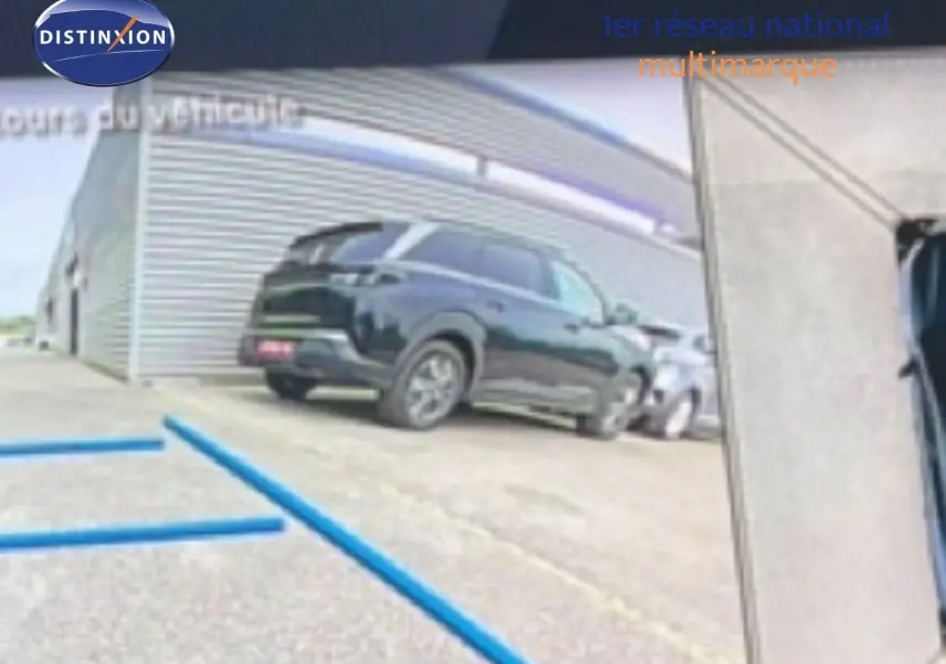 Vue 3/4 arrière d’un Peugeot 408 Hybrid 145ch GT noir métal garé devant un bâtiment industriel.