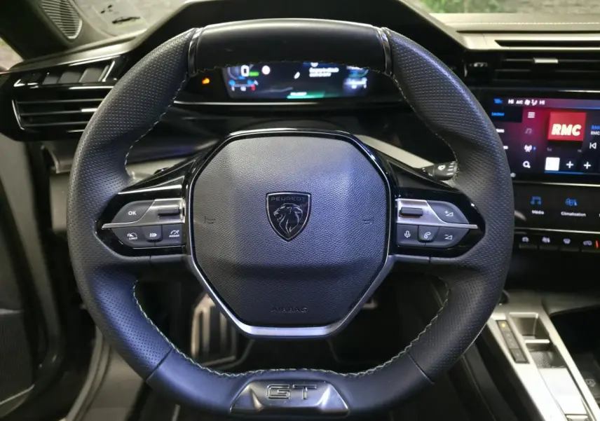 Vue rapprochée du volant cuir perforé noir avec badge GT et tableau de bord numérique de la Peugeot 408 2025.