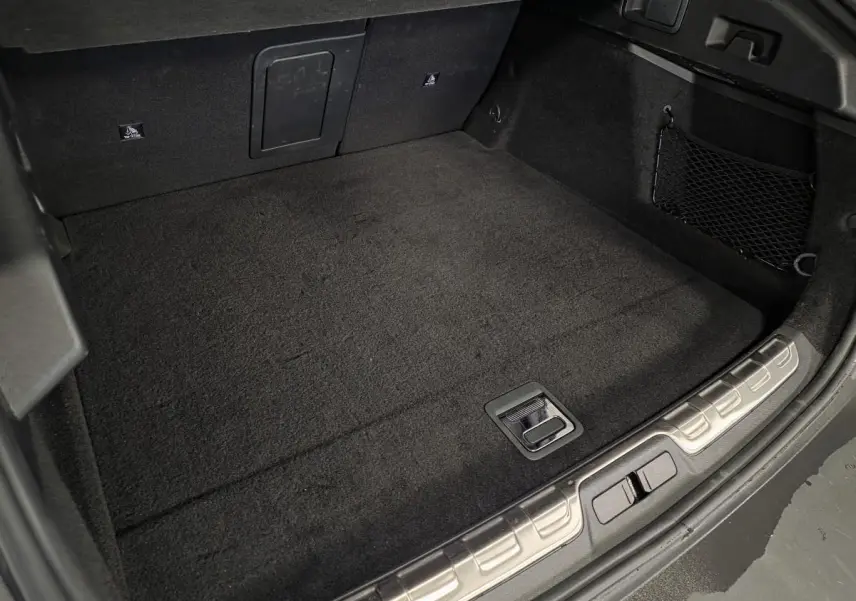 Coffre spacieux et propre du hayon arrière d'une Peugeot 408 gris, avec tapis noir et filet de rangement latéral.