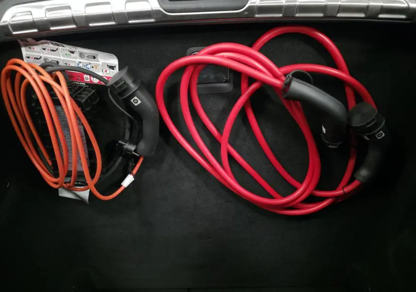 Coffre ouvert du Peugeot 408 gris avec câbles de recharge rouge et orange rangés sur le tapis noir.