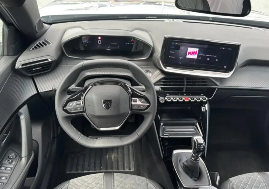 Vue intérieure frontale du tableau de bord et volant noir du Peugeot 2008 1.2 100 allure avec écran tactile et levier de vitesse manuel.
