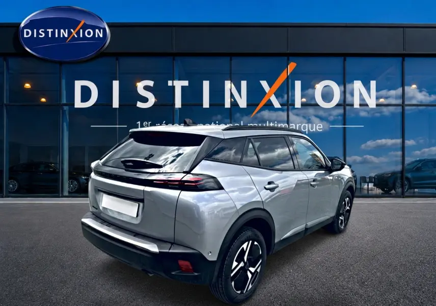 Peugeot 2008 gris artense en 3/4 arrière droit, avec jantes alu et feux arrière LED visibles devant showroom Distinxion.