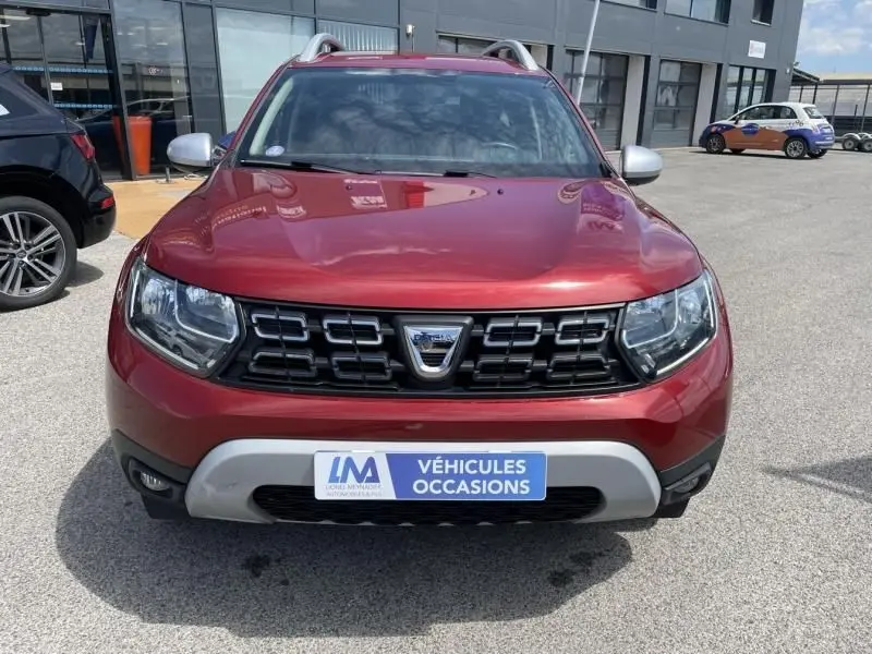Vue avant d'un Dacia Duster rouge métal 2020 avec calandre noire et plaque "Véhicules Occasions" visible.