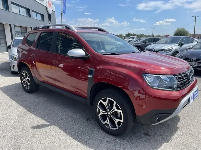 Dacia Duster TCE 150 Prestige 4x2 rouge métal vu en 3/4 avant côté gauche, avec jantes alliage et rétroviseurs argentés.