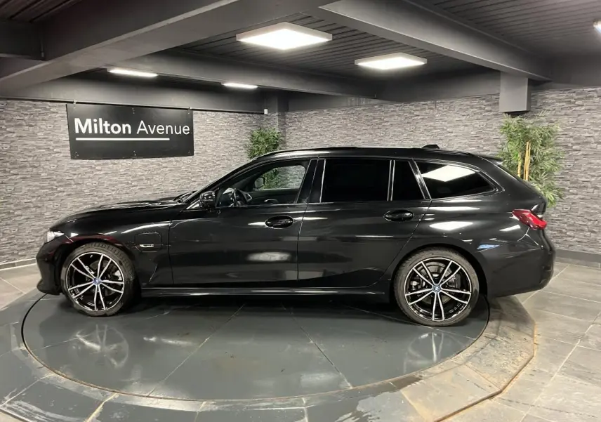 BMW Série 3 320e Touring noire vue de profil côté gauche avec jantes M Sport bicolores en intérieur showroom.