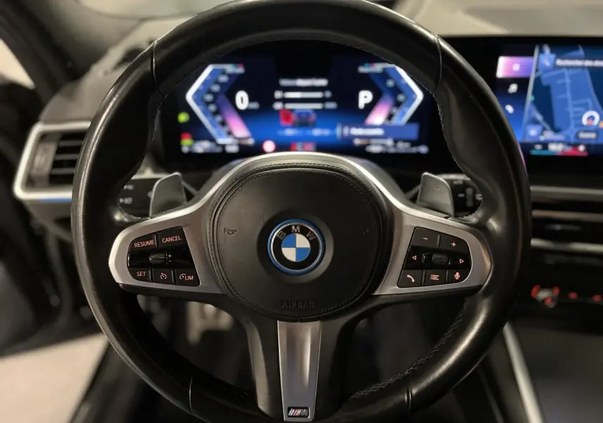 Volant M cuir noir BMW en gros plan avec tableau de bord numérique et écran de navigation en arrière-plan.