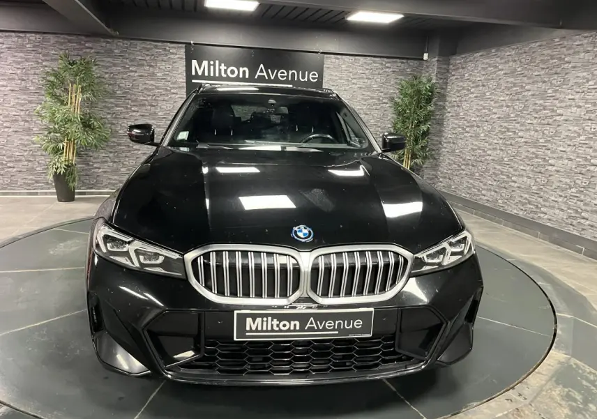 Vue frontale d'une BMW Série 3 G21 320e Touring noire avec calandre double haricot et phares LED dans un showroom.